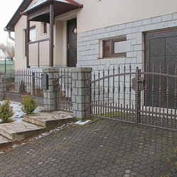 Schmiedeeiserne Umzäunung eines Einfamilienhauses – geschmiedeter Zaun mit verdichteten Elementen im unteren Teil 