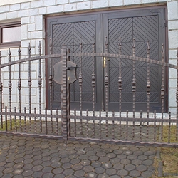 Schmiedeeiserner Zaun an einem Einfamilienhaus mit verdichteten Elementen im unteren Teil 