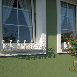 A wrought iron flowerpot holder for a window